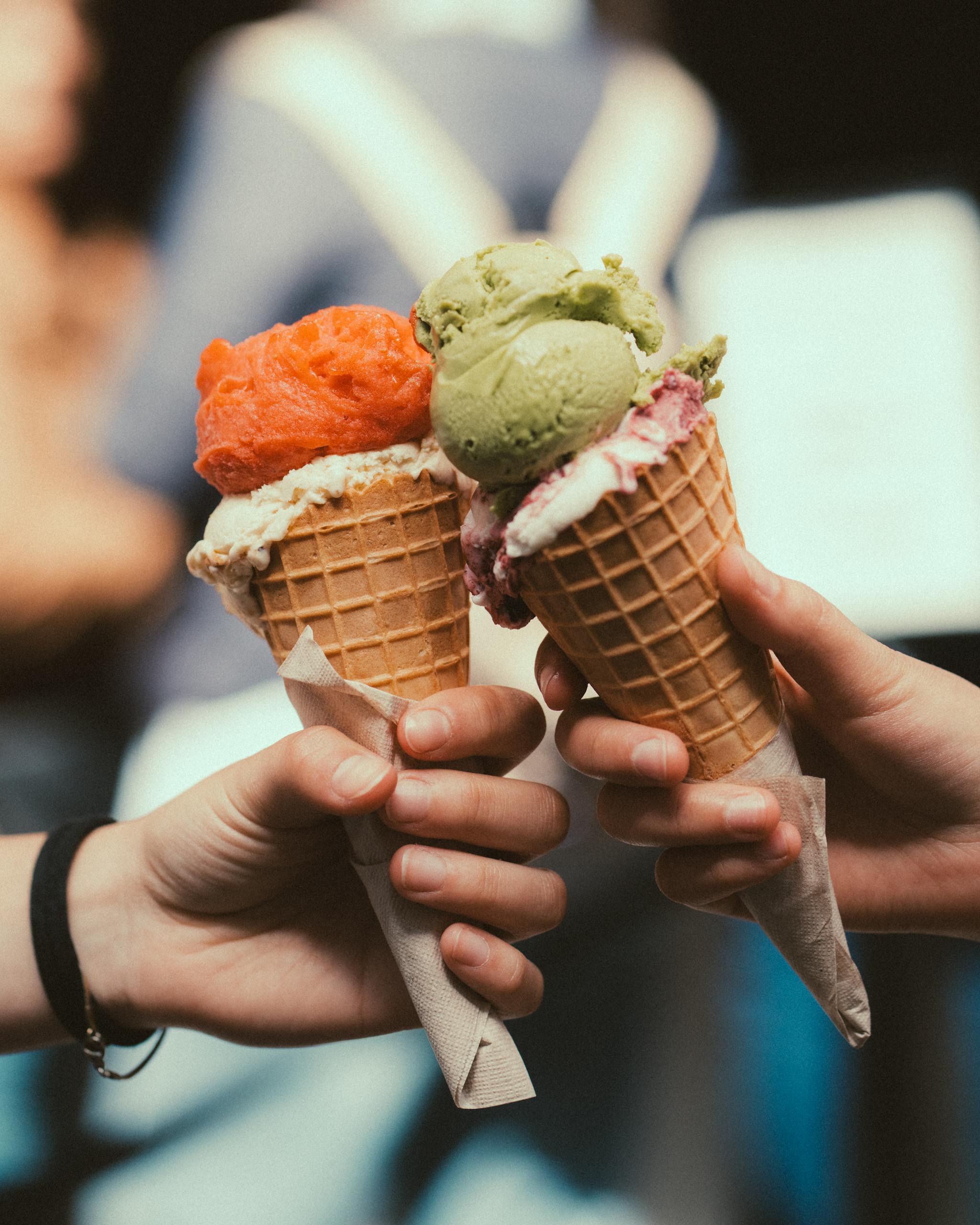 Close-up of three vibrant ice cream cones held by hands, outdoors.
